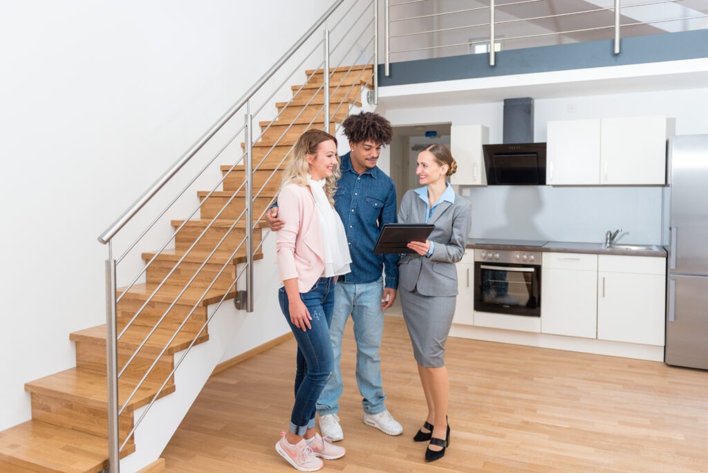 Young couple discusses home purchase with a real estate agent in a modern kitchen, highlighting the property’s attractive features and layout.