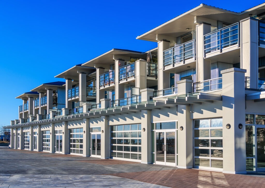 Modern building facade featuring several upper-floor balconies and large glass doors, set against a clear blue sky, highlighting contemporary architecture.