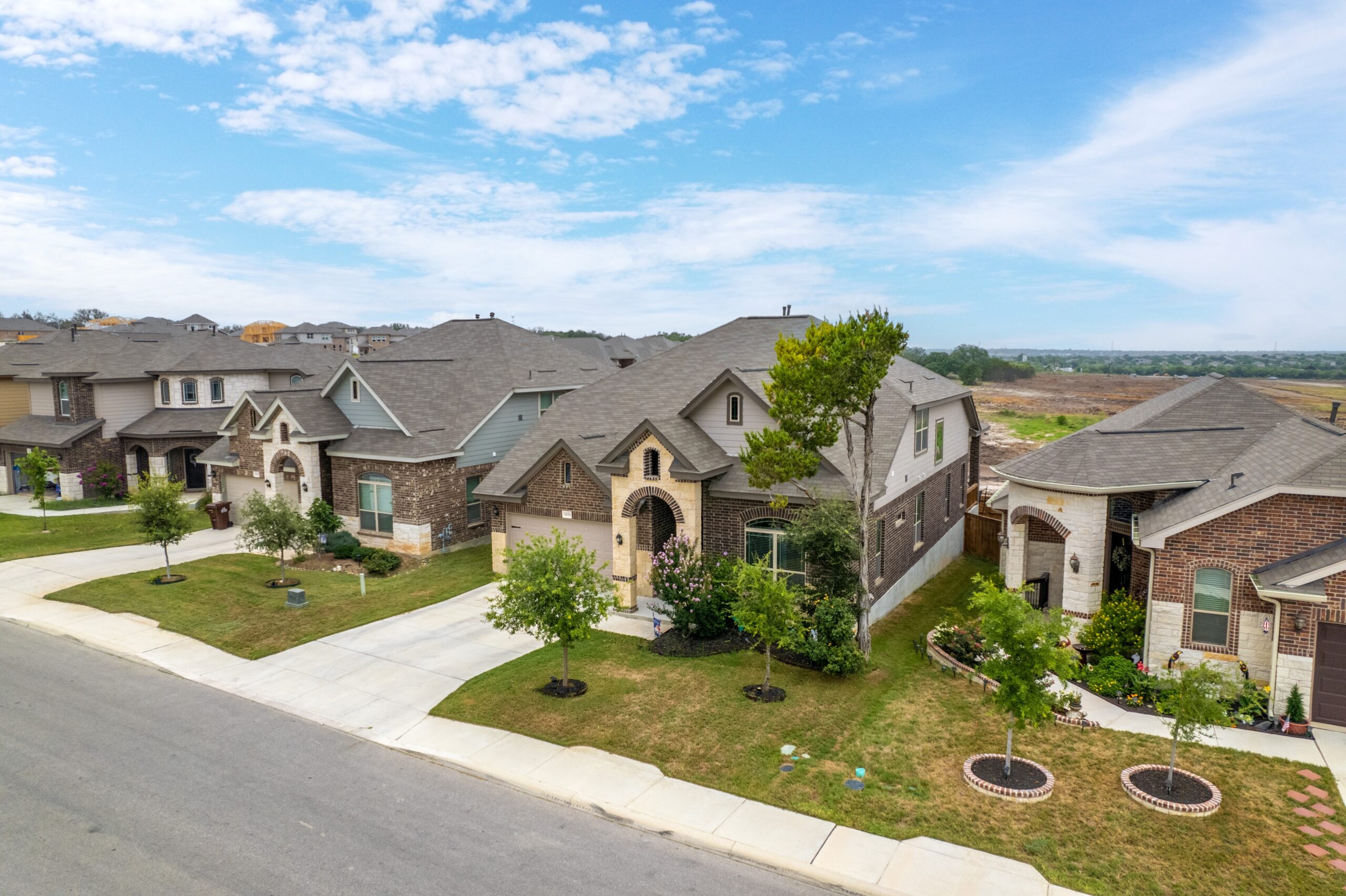 Residential neighborhood showcasing modern homes with landscaped yards and a clear blue sky. Houses have varied architectural styles and neat pathways.